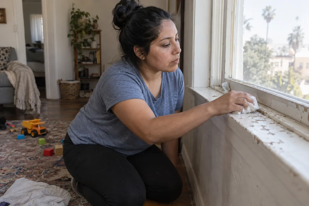Madre limpia pedazos de pintura vieja de la ventana cerca de los juguetes de su hijo